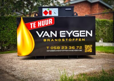 Op de foto zien we een zwarte werftank met reclame van Brandstoffen Van Eygen. Deze staat voor een woning op een verhard stuk grond. Errond zien we enkele grasvelden.